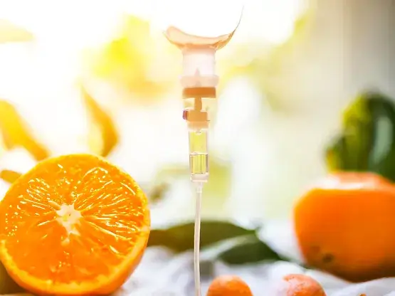 A vitamin IV drip next to fresh oranges, symbolizing vitamin C infusion amidst a sunlit, natural background with blurred greenery.